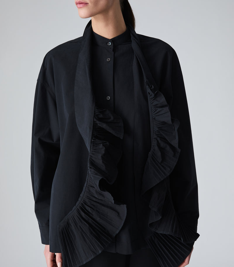 A model wearing a black long-sleeve blouse with a black scarf that has a dramatic pleated ruffle trim on both ends, displayed flat against a light gray background.