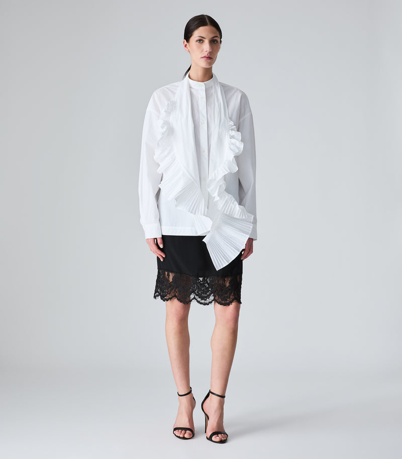Woman wearing a white blouse with ruffles and a black lace skirt on a gray background