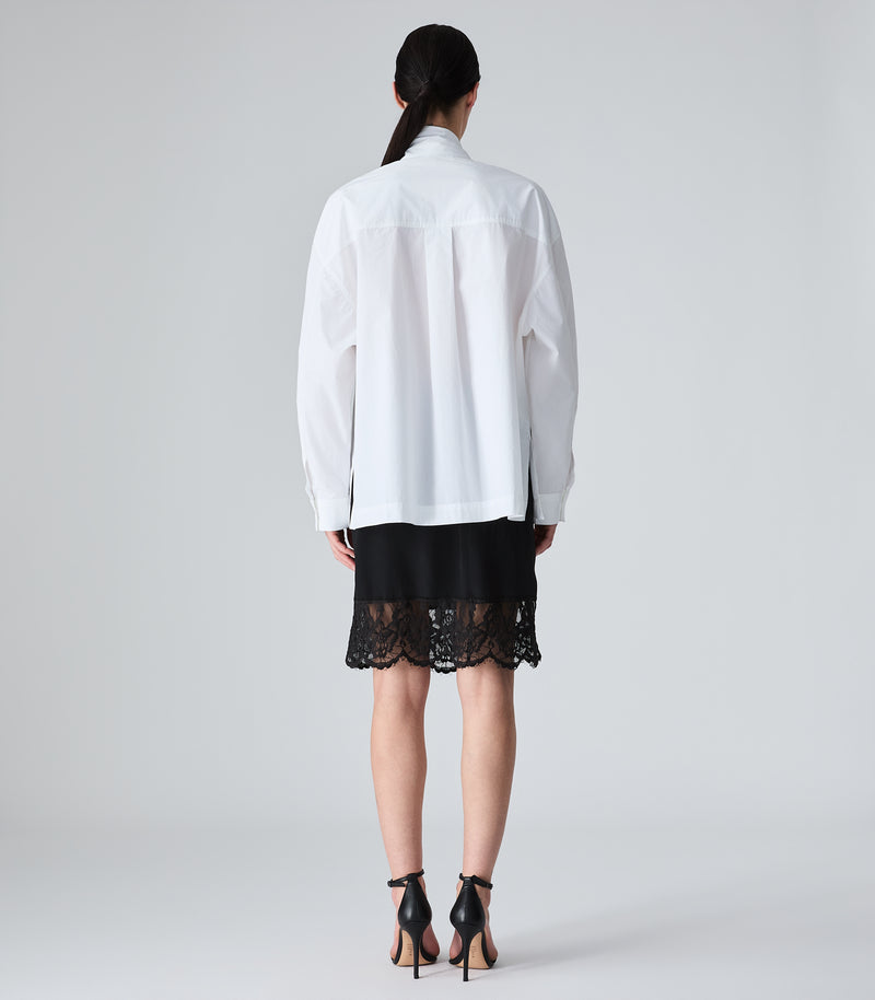 Person wearing a white blouse and black lace skirt on a plain background