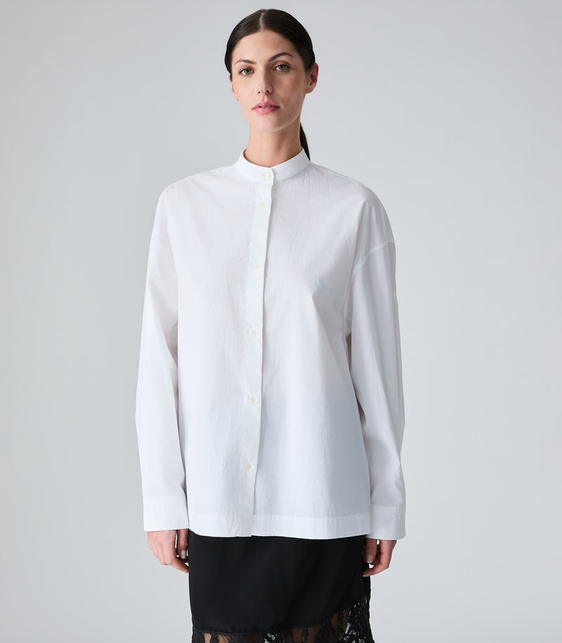 Woman wearing a white shirt with a high mock neck against a plain background
