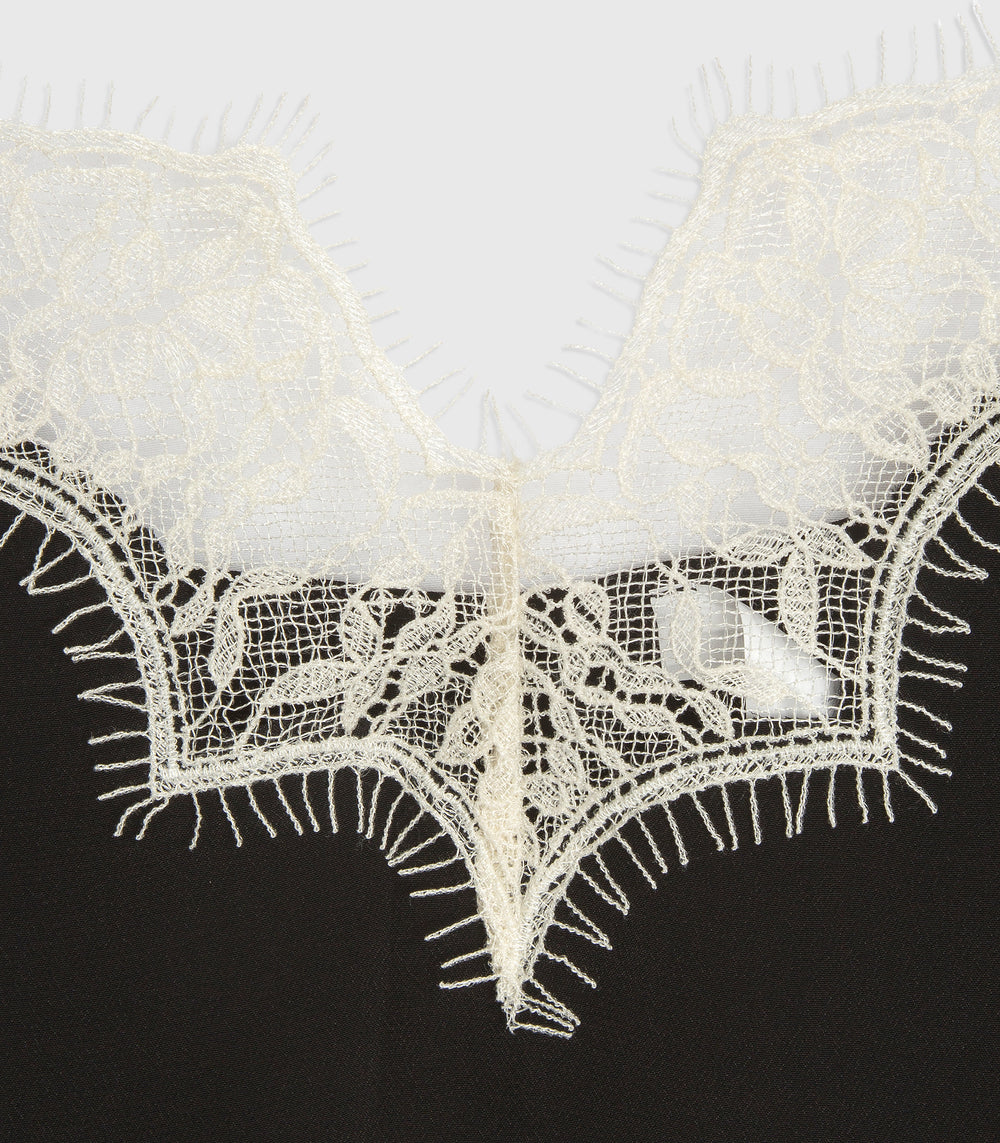 Close-up of a white floral lace trim with fringed edges, layered over a black fabric background.