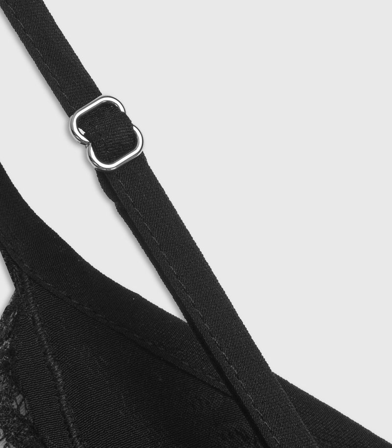 Close-up of a black bra strap with a silver metal adjustment buckle on a light gray background.