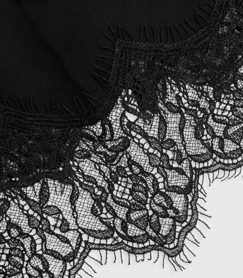 Close-up of a black lace textile with floral lace pattern and fringed edges over a plain light background.