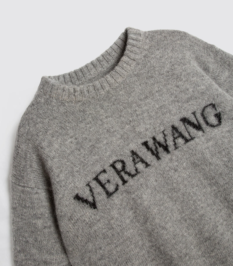 Close-up of a heather gray knit sweater with the brand name 'VERAWANG' knitted in black across the chest, shown on a light gray background.