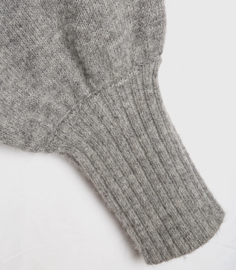 Close-up of a gray knit garment showing a ribbed cuff and soft textured fabric on a plain white background.