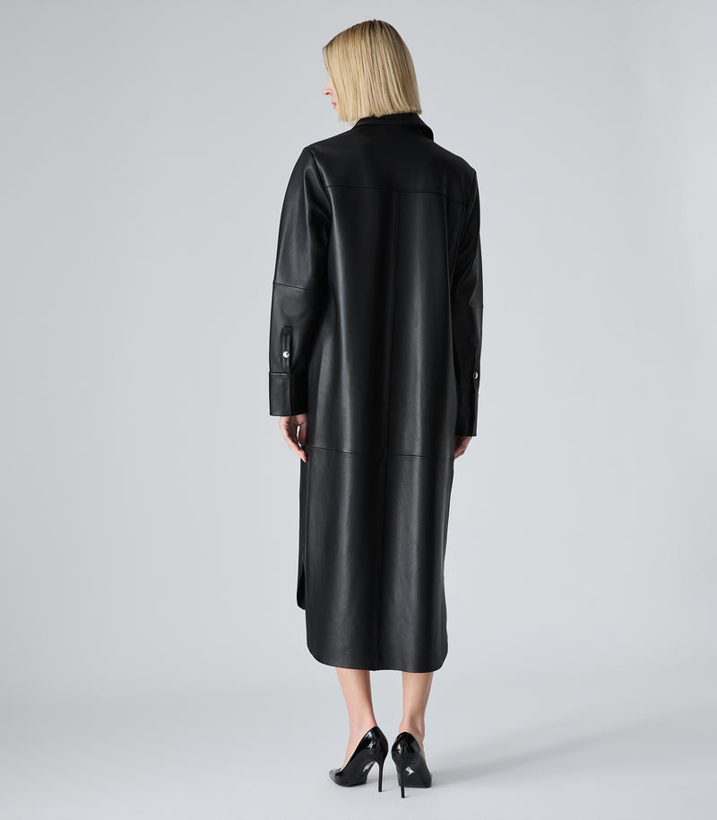 A woman viewed from the back wearing a long black leather coat with structured shoulders and black high heels, standing against a light gray studio background.