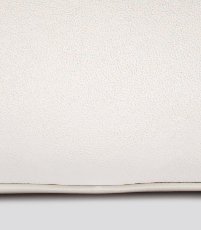 A close-up of a off-white pebbled leather bag with a thin horizontal seam visible along the bottom edge against a neutral light gray background.