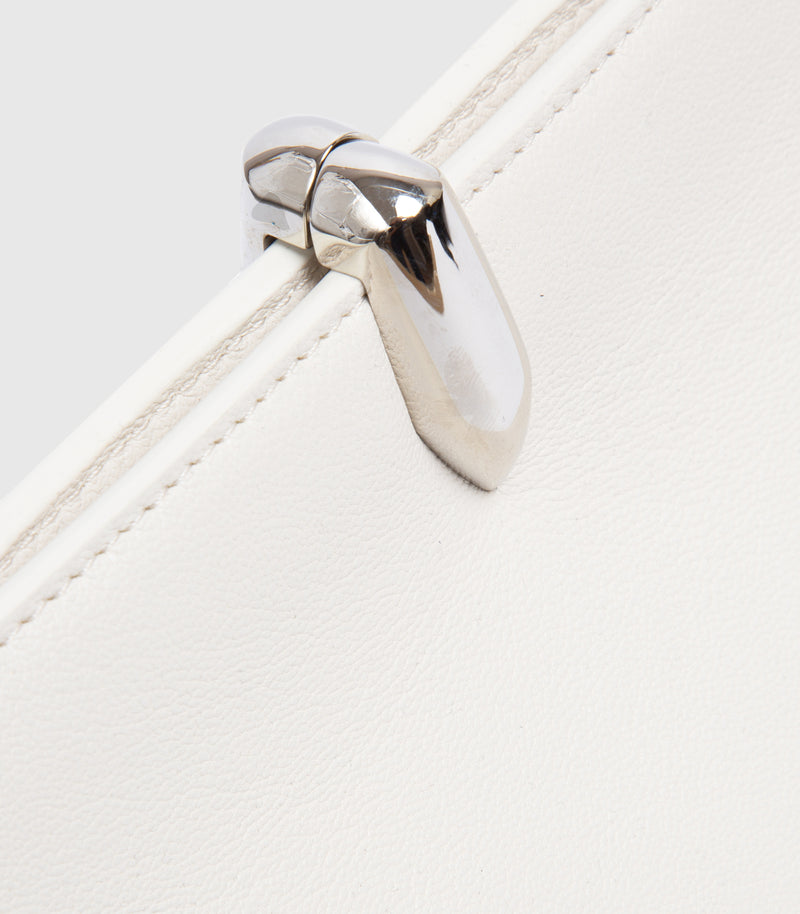 Close-up of a white leather bag featuring a polished silver metal clasp and fine stitching along the edge.