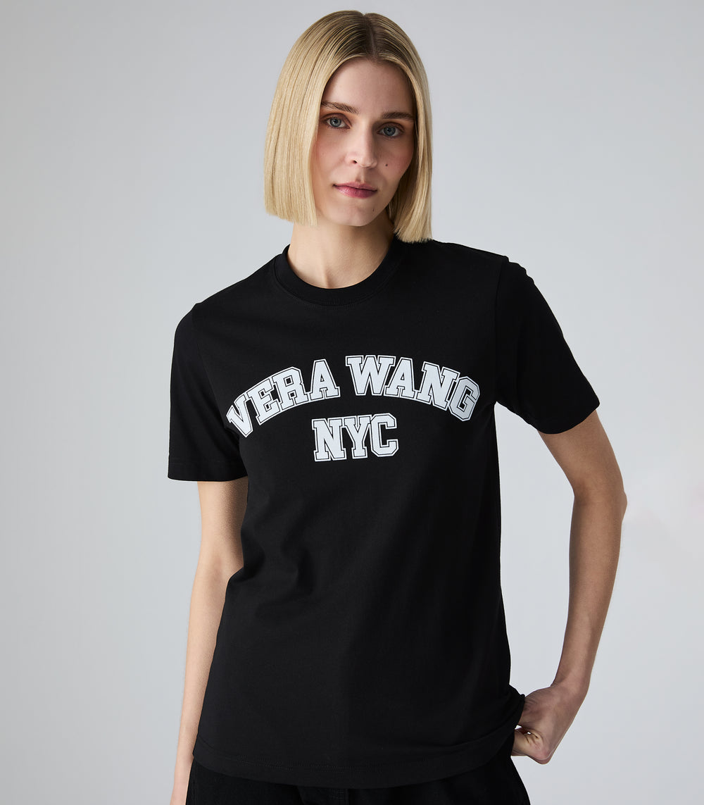 A closer shot of a Female model wearing a slim-fit black t-shirt with 'VERA WANG NYC' spell-out logo across the front, against a white background.