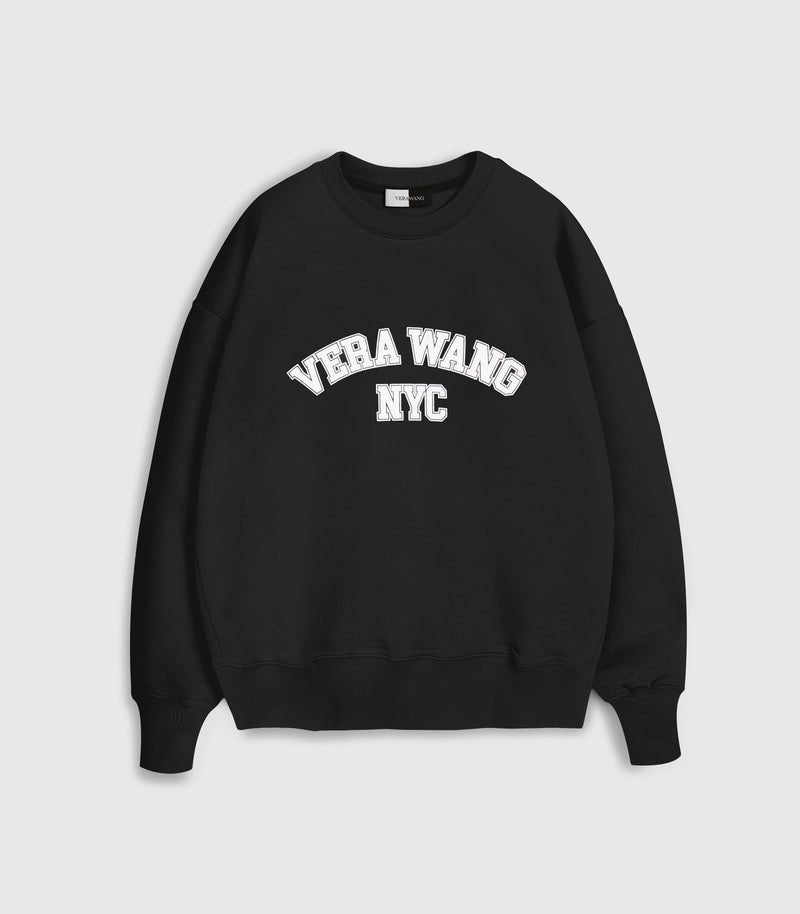 Flat lay product view of a relaxed-fit black crewneck sweatshirt featuring an arched varsity-style 'VERA WANG NYC' graphic printed in white block lettering with a subtle outline across the chest, complete with a ribbed collar, hem, and cuffs against a light grey background.