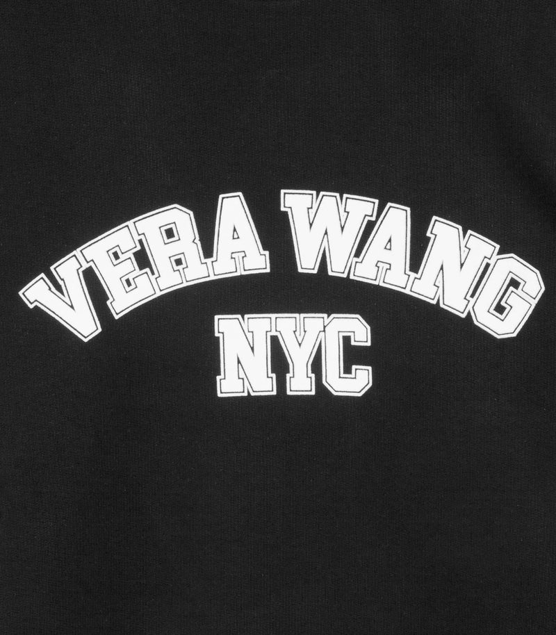 A high-contrast, close-up product shot focusing on the chest graphic of a black sweatshirt, showcasing the white printed 'VERA WANG' text arched over 'NYC' in a bold, outlined collegiate varsity block font.