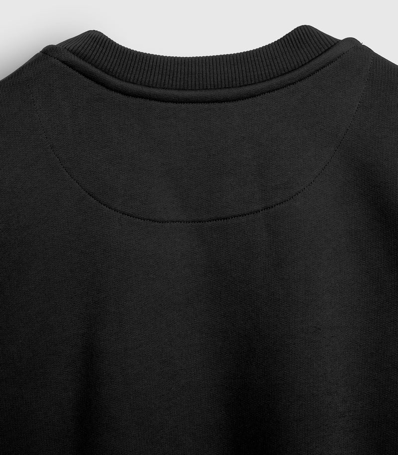 Close-up product view of the back of a black crewneck sweatshirt, showcasing the premium ribbed knit collar, clean tonal stitching, and a decorative crescent-shaped half-moon yoke seam below the neckline against a light grey background.