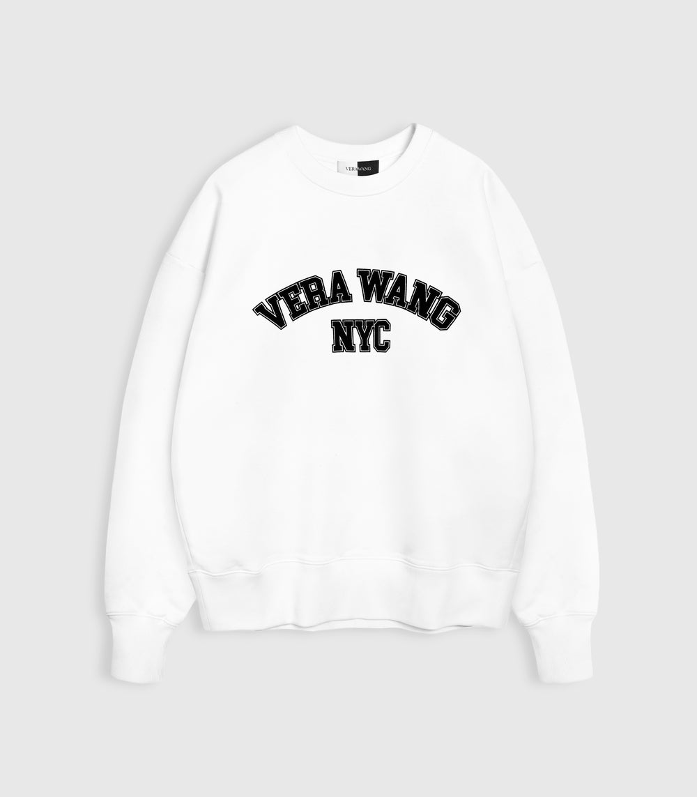 Flat lay product view of an oversized white crewneck sweatshirt featuring 'VERA WANG NYC' in black block varsity lettering arched across the front, complete with ribbed cuffs and hem against a white background.