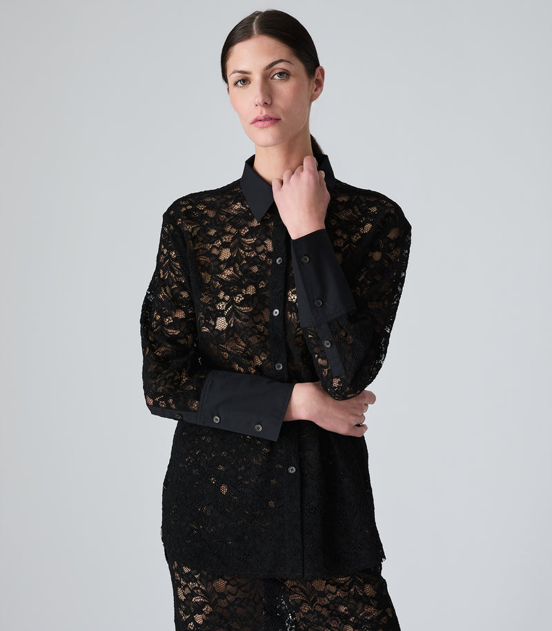 A woman modeling a black long-sleeve lace button-up shirt with solid black collar, cuffs, and button placket, photographed against a light gray studio background.