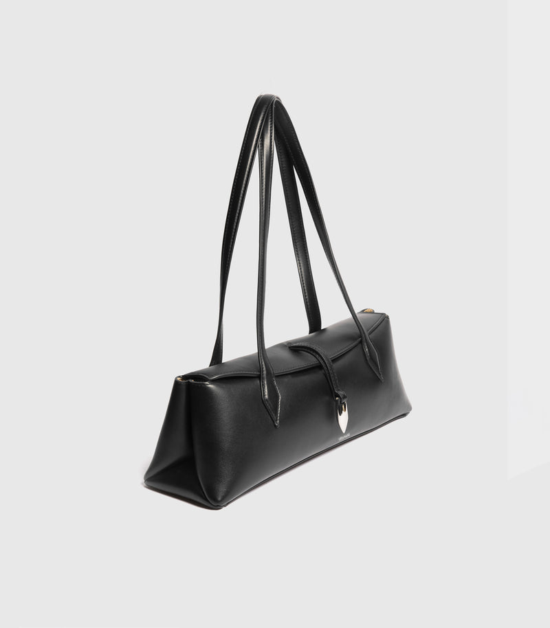 A black leather shoulder bag with a long strap and a small silver-tone shield charm, shown from a side angle on a light gray background.