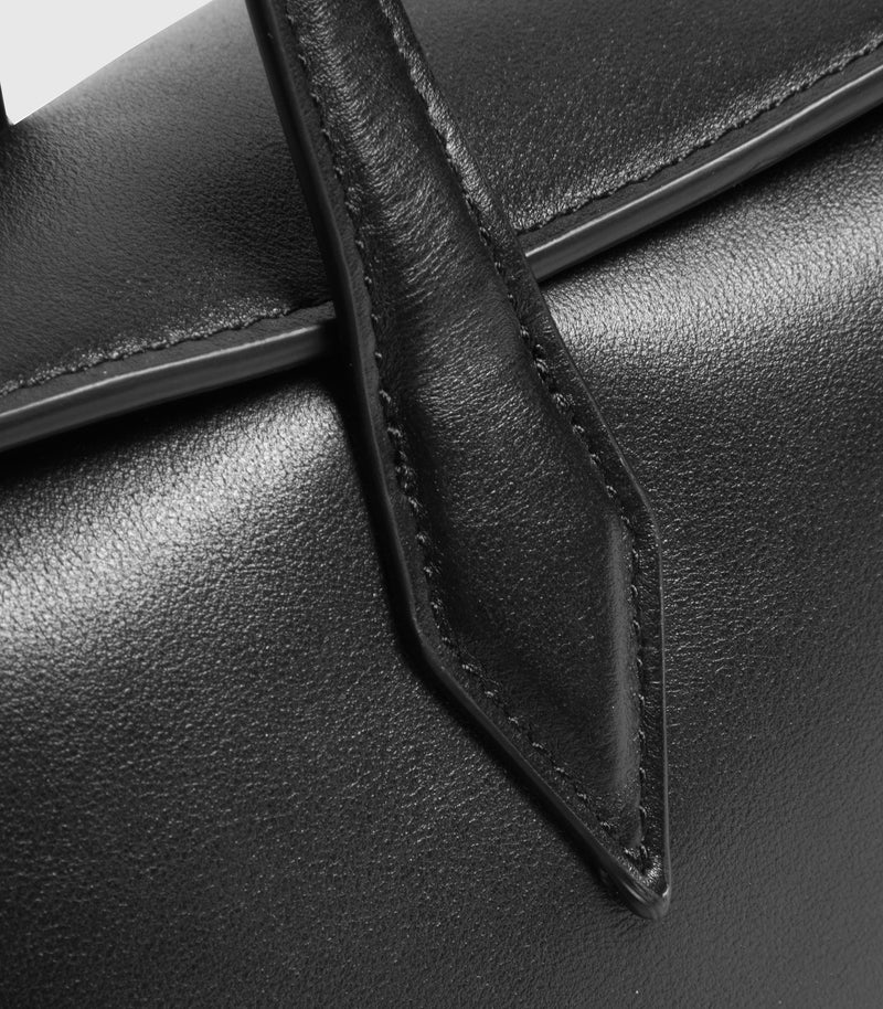 Close-up of a black leather handbag showing the texture of the leather and a pointed stitched strap detail.