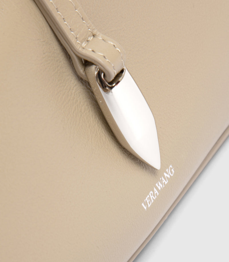 Close-up of a beige leather bag with a pointed silver metal accent and visible VERA WANG branding on the surface.