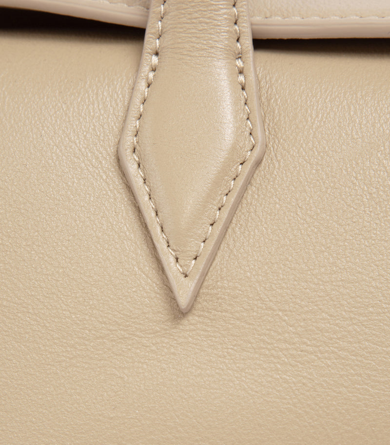 Close-up of a light beige leather handbag showing a pointed leather tab with decorative contrast stitching.