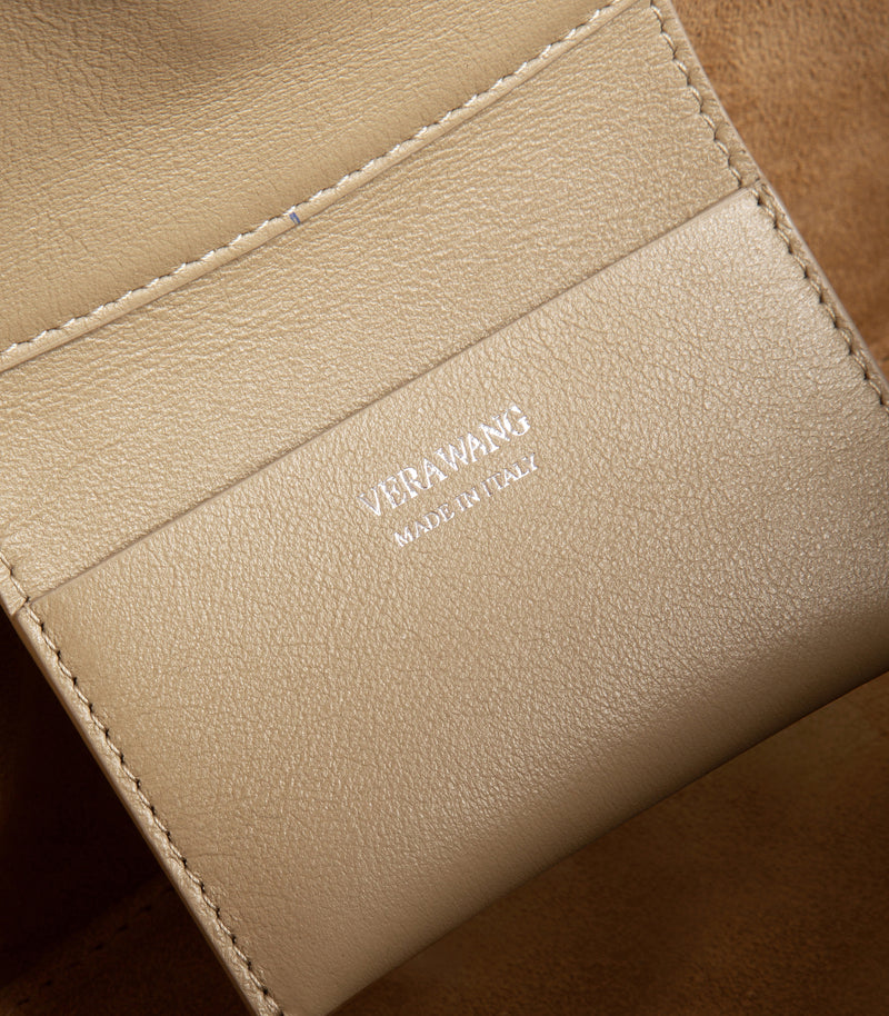 Close-up of a beige leather bag with visible stitching and debossed branding reading 'VERA WANG MADE IN ITALY'.