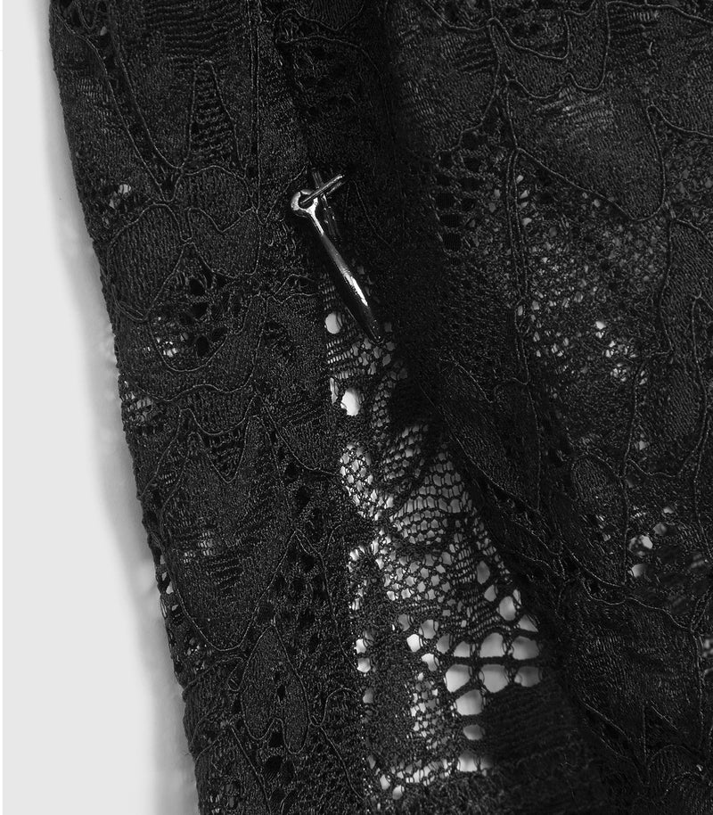 Macro close-up product view of a black lace legging ankle cuff, showcasing a functional concealed zip fastening at the inner hem. The image highlights the fine floral lace mesh patterns and the small, matte black teardrop-shaped puller protruding from the stitched lower edge, set against a plain light grey backdrop.