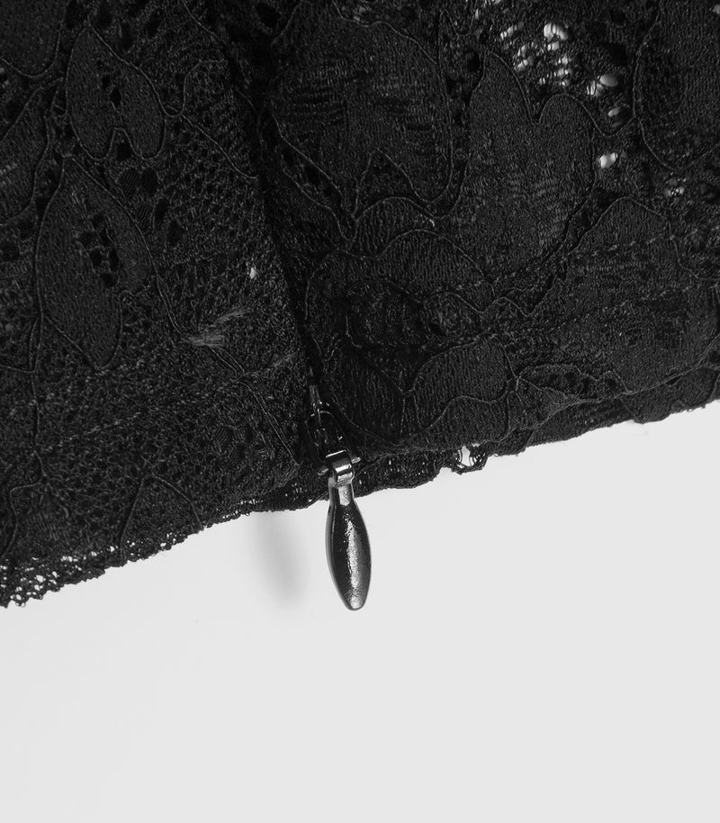 Close-up product view of a black lace legging ankle cuff, showcasing a functional concealed zip fastening at the inner hem. The image highlights the fine floral lace mesh patterns and the small, matte black teardrop-shaped puller protruding from the stitched lower edge, set against a plain light grey backdrop.