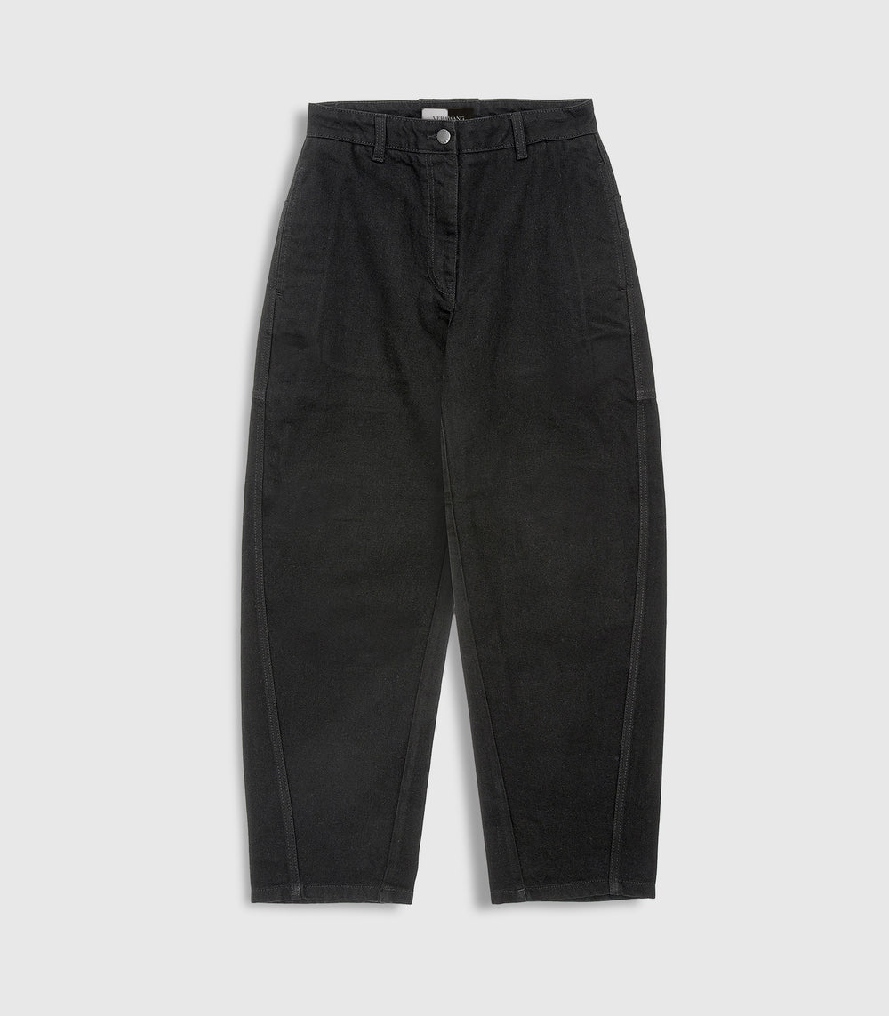 Flat lay product view of high-rise, ankle length balloon jeans in washed black denim, showcasing structured, curved side-seam detailing and a silver button closure against a light grey background.