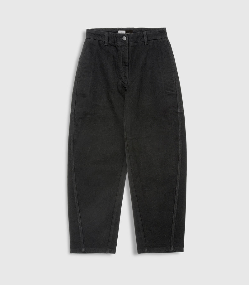 Flat lay product view of high-rise, ankle length balloon jeans in washed black denim, showcasing structured, curved side-seam detailing and a silver button closure against a light grey background.