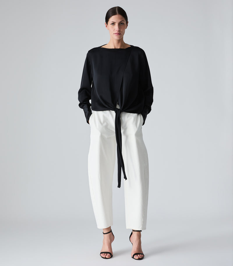 Woman wearing a black top and white pants on a gray background