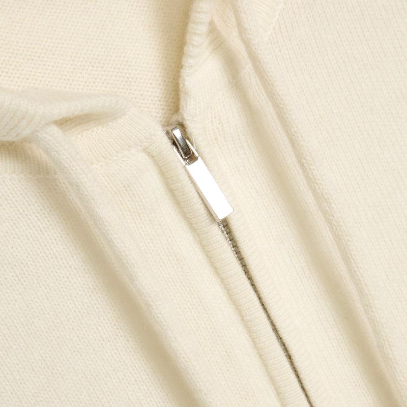 Close-up of a cream-colored zip-up hoodie showing the ribbed knit fabric and a silver metal zipper pull.