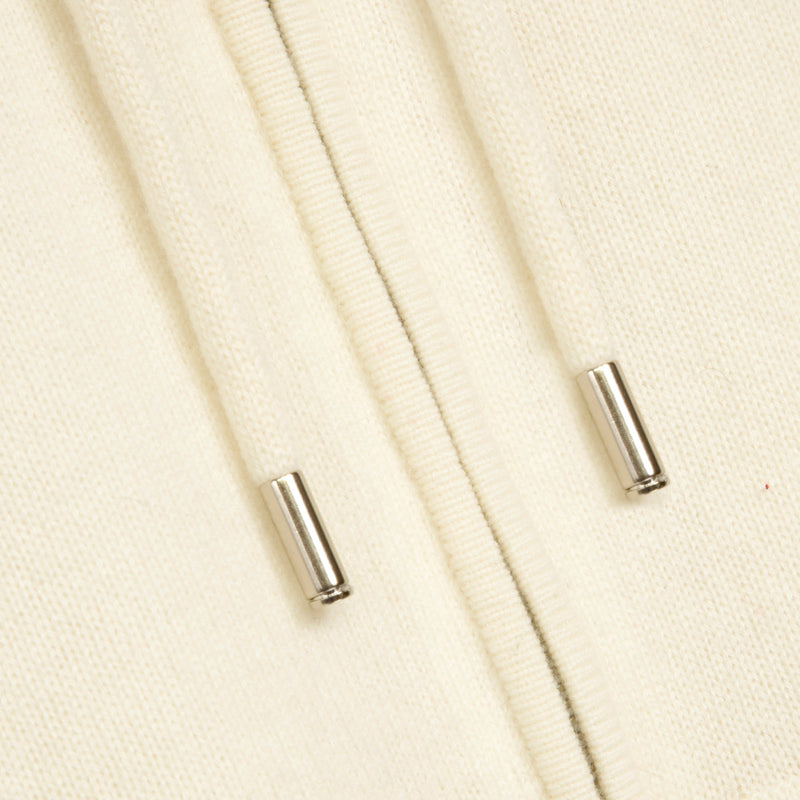 Close-up of a cream-colored knit fabric with two small silver metal cylindrical accents on a matching textile surface.