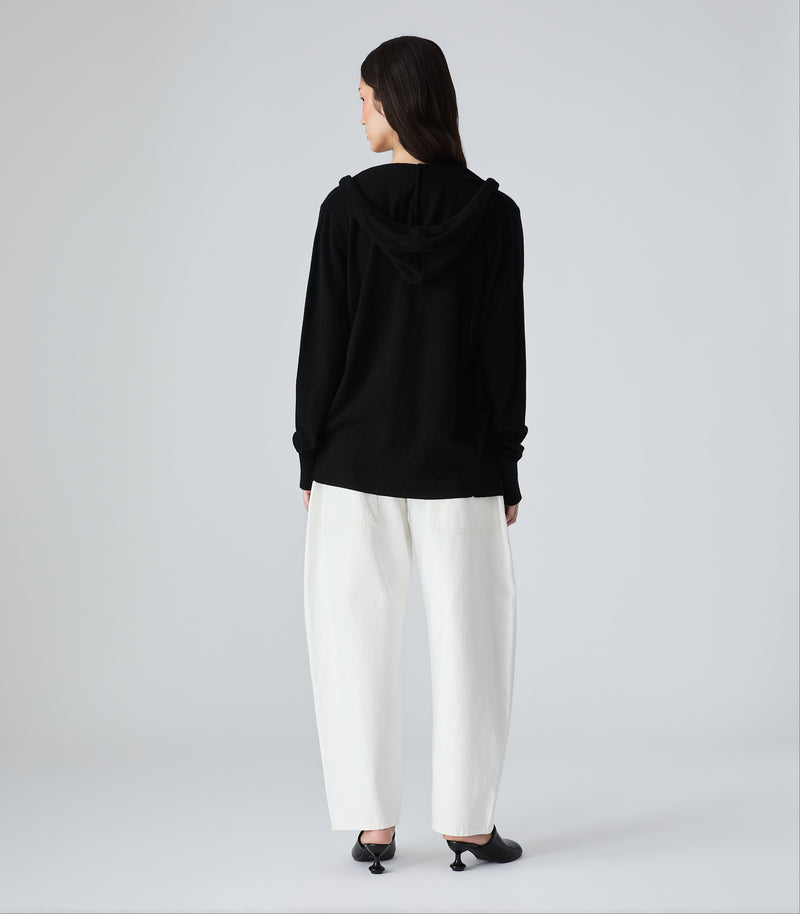 Person wearing a black hoodie and white pants on a gray background