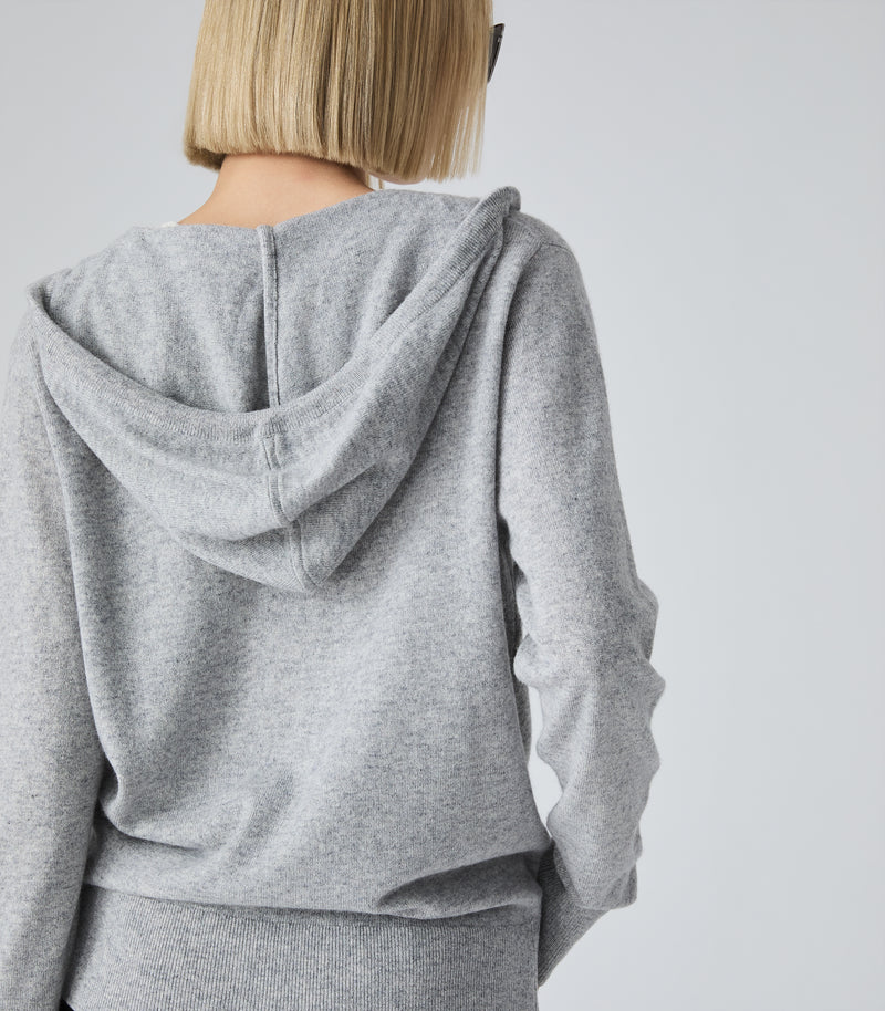 A person shown from the back wearing a heather gray hooded sweatshirt and matching gray bottoms against a plain light gray studio background.