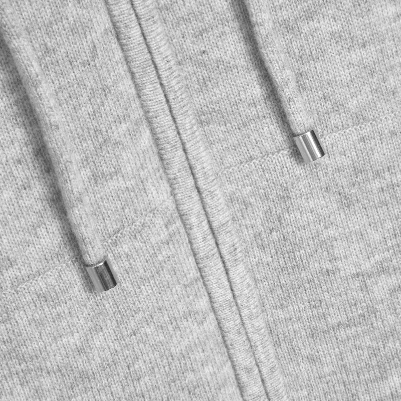 Close-up of a light heather gray zip-up hoodie showing the ribbed knit fabric, drawstring cords, and silver metal tip ends.