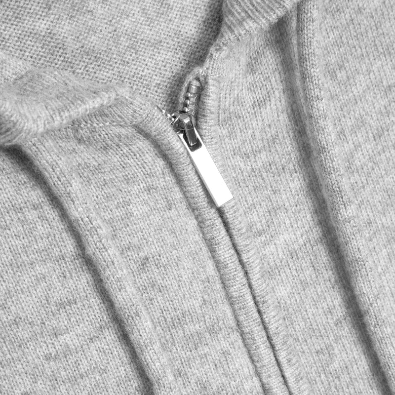 Close-up of a light gray ribbed knit garment with a silver zipper and white pull tab.