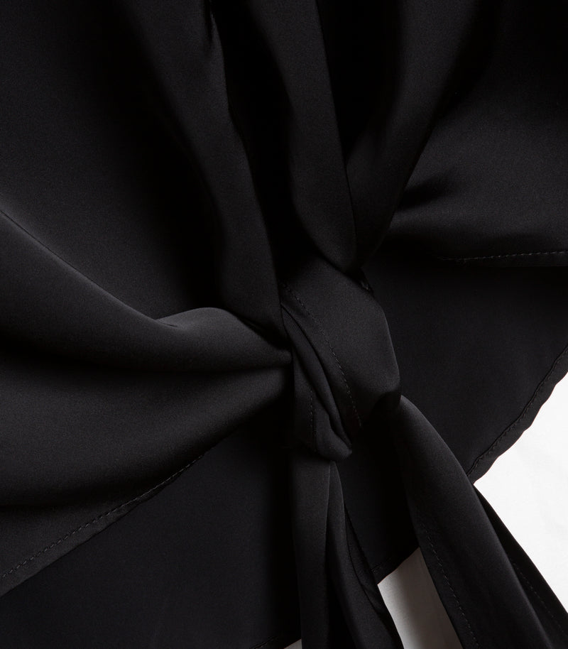 Close-up of a black draped fabric with a gathered knot detail and visible stitching, shown against a small white background area.
