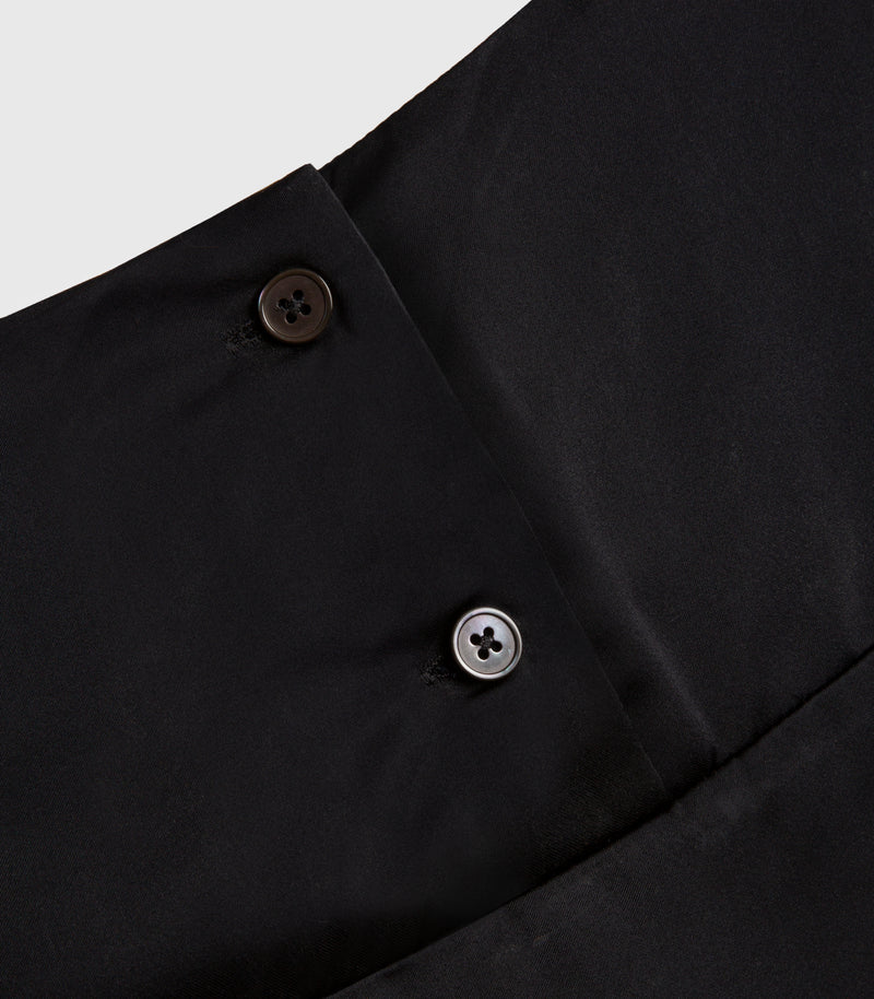 Close-up of a black garment showing a buttoned collar or placket with two buttons, one dark brown and one silver, on a light gray background.