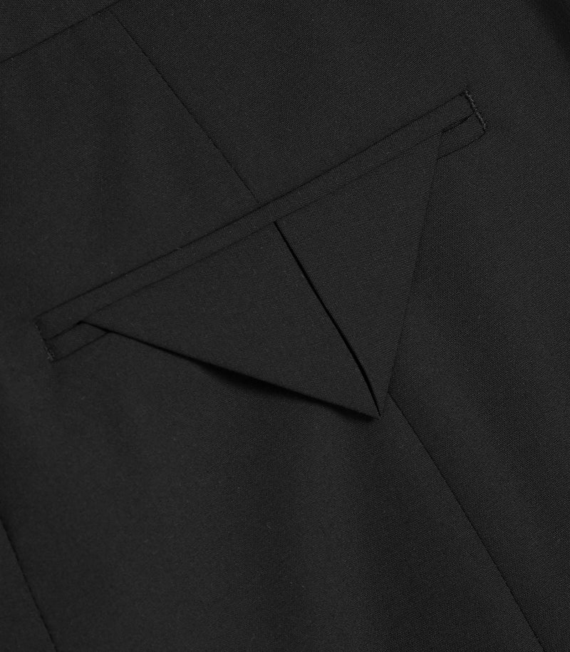 Close-up of a black tailored garment showing a triangular pocket flap and fine fabric texture.