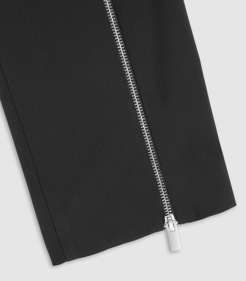 Close-up of a black garment with a prominent silver zipper running diagonally across the frame, set against a light gray background.