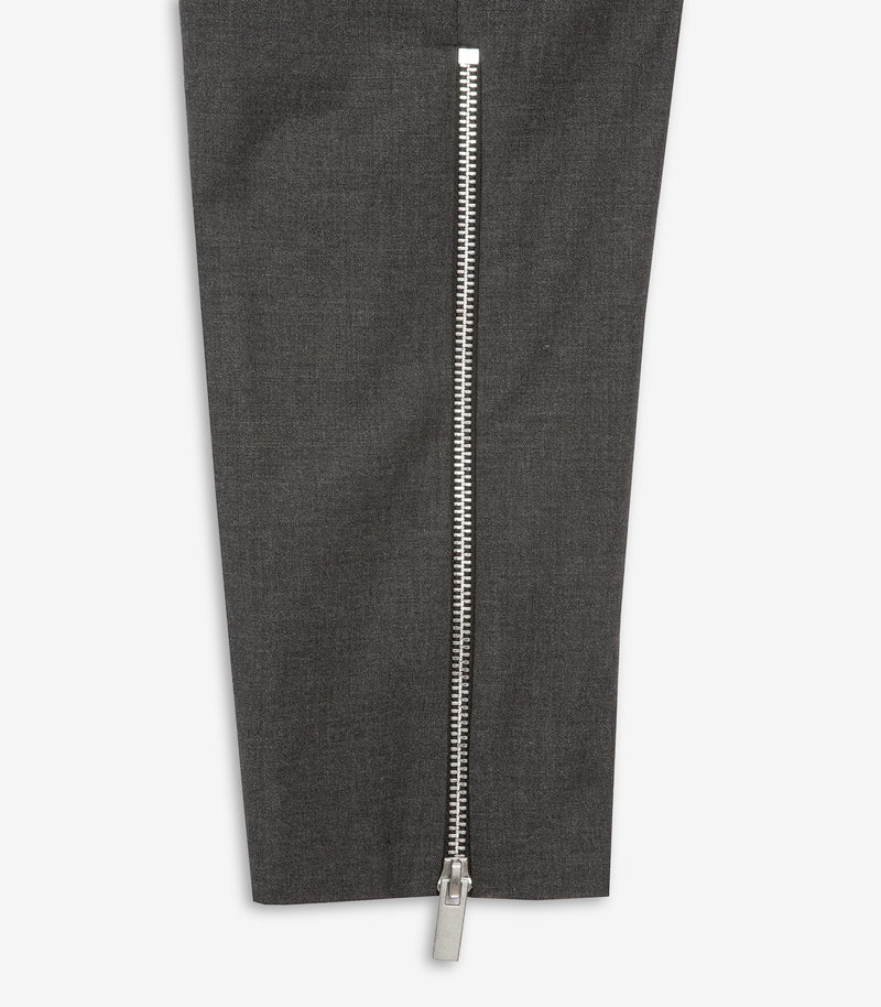 Close-up of dark gray textured trousers with a prominent silver metal zipper running down the front of the leg.