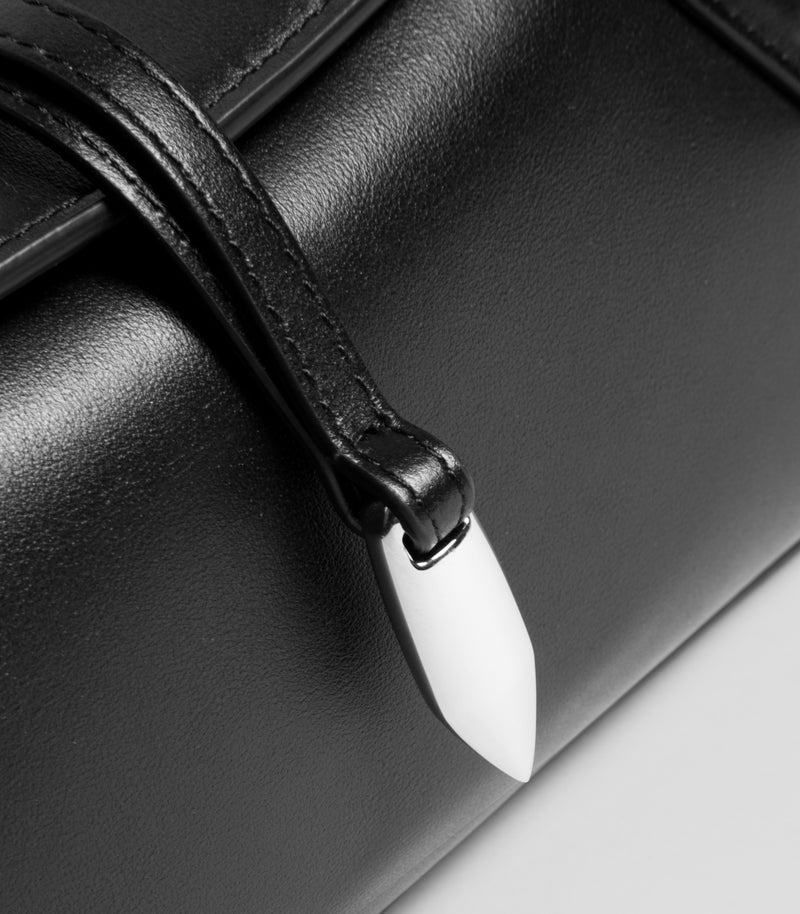 Close-up of a black leather handbag with a strap and a glossy white teardrop-shaped metal accent.