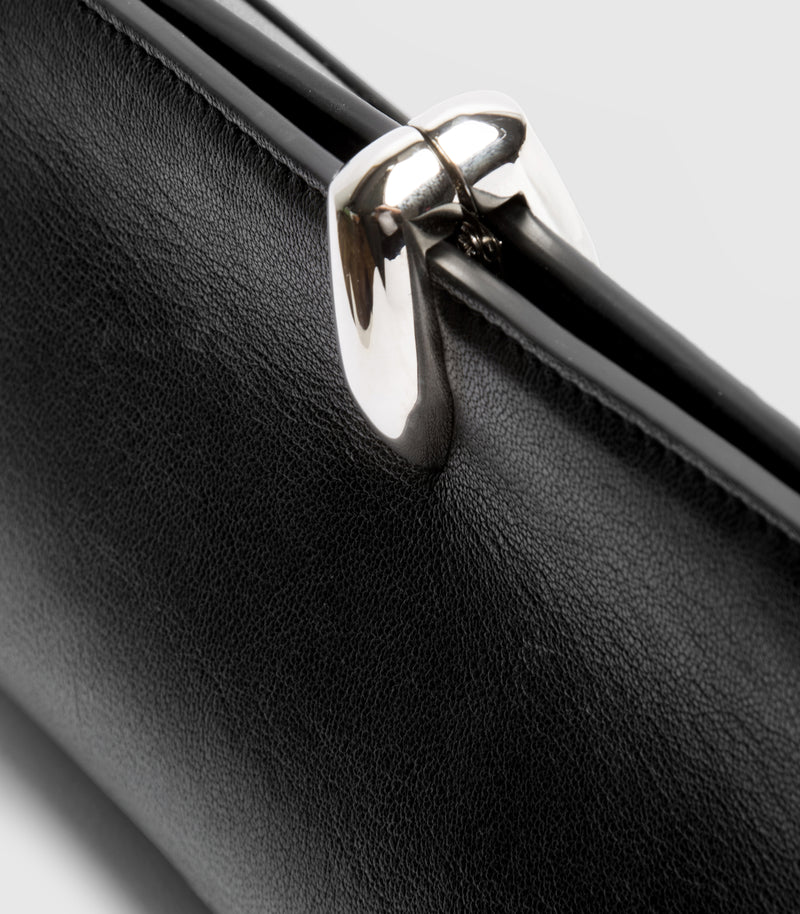 Close-up of a black leather clutch bag featuring a prominent, polished silver-tone metal clasp on a light gray background.