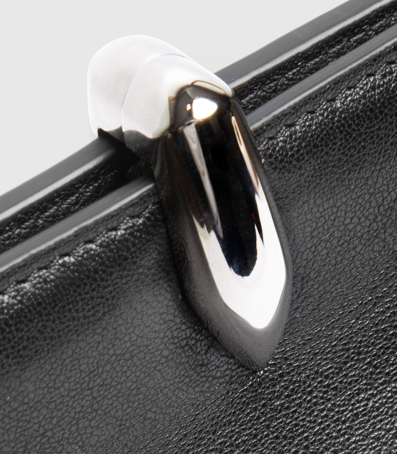 Close-up of a black textured leather bag with a glossy silver metal clasp on a light gray background.