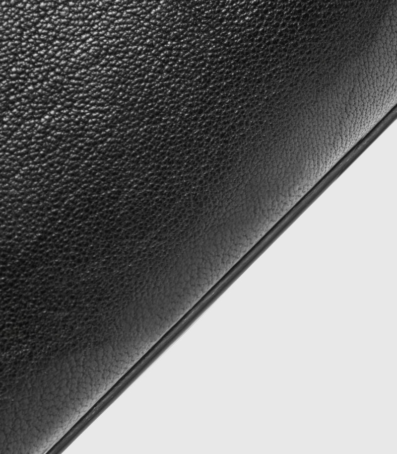 Close-up of a black pebbled leather bag with a thin dark edge and a light gray background visible in the lower right corner.