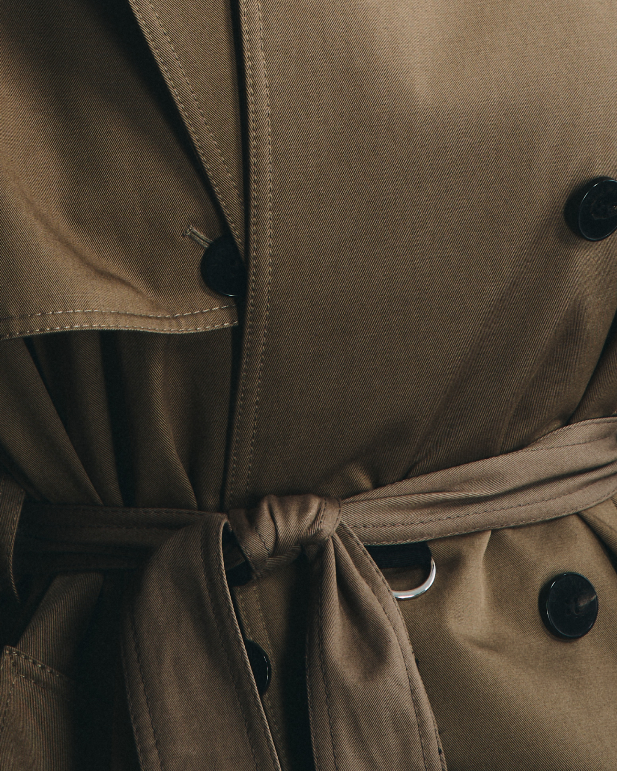 Close-up of a brown trench coat with black buttons and belt.