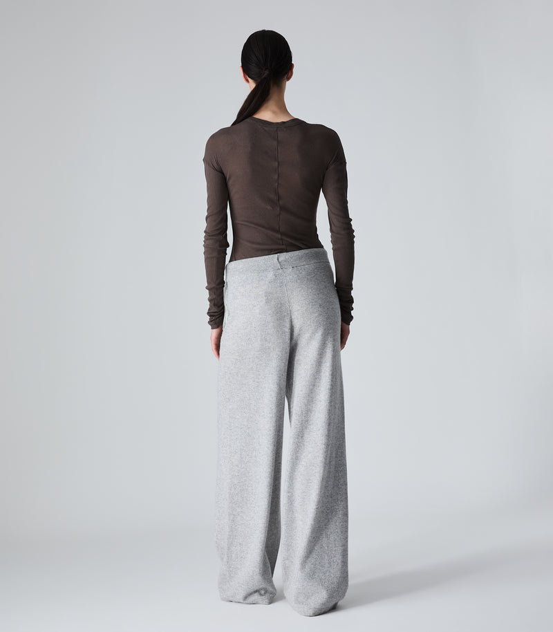 A model shown from the back wearing a dark brown long-sleeve top and light gray wide-leg sweatpants against a light gray studio background.