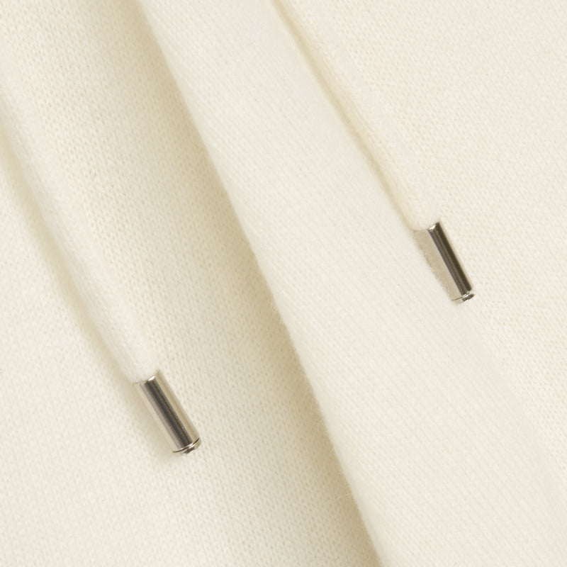 Close-up of a cream-colored knit fabric with two metallic silver drawstring tips visible.