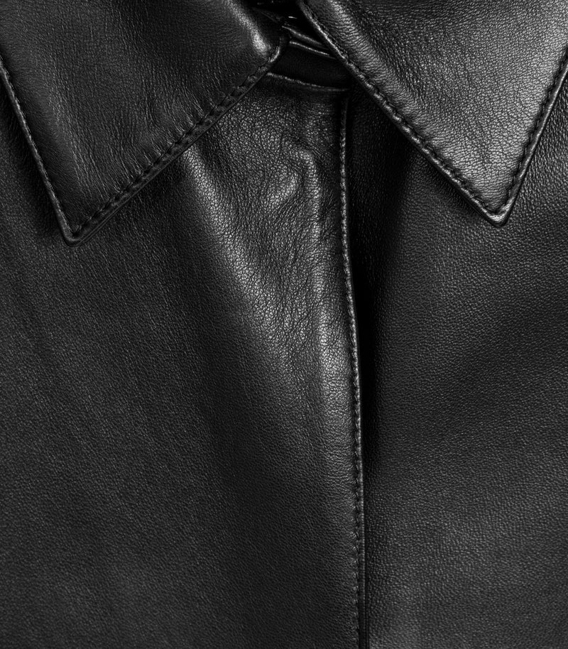 Close-up of a black leather jacket showing the collar, fine grain texture, and detailed stitching.