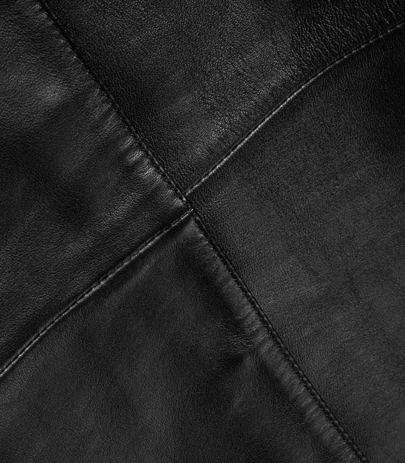 Close-up of black leather jacket with visible grain and diagonal stitched panel seams.
