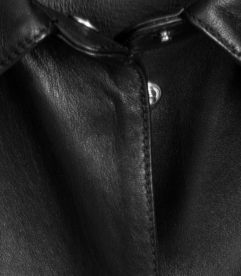 Close-up of a black leather jacket showing the collar, button closure, and fine leather grain texture.