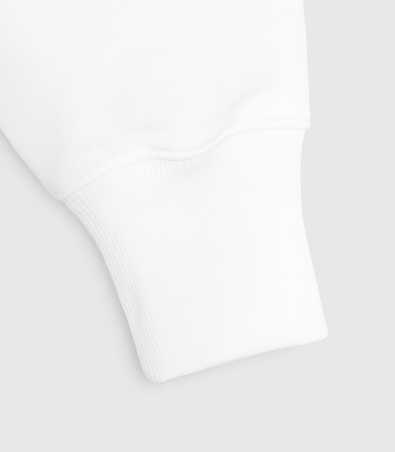 Close-up product view of a white crewneck sweatshirt, highlighting the clean construction of the ribbed sleeve cuff, the soft fleece fabrication, and the tonal stitching along the wrist seam against a light grey background.